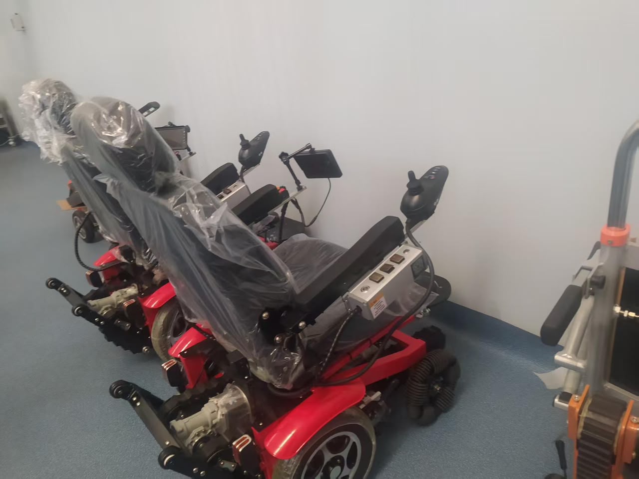 Finished Movo X units in the QC bay — red powered stair-climbing wheelchairs with joystick controllers, tracks and battery packs, wrapped in protective film ready for final testing